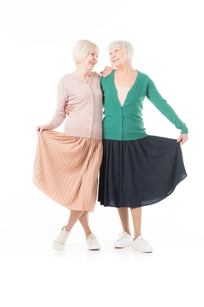 Smiling stylish senior women holding skirts isolated on white — Stock Photo
