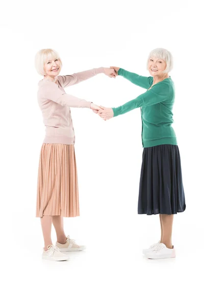 Zwei stylische Seniorinnen, die einander die Hand reichen, isoliert auf weißem Grund — Stockfoto