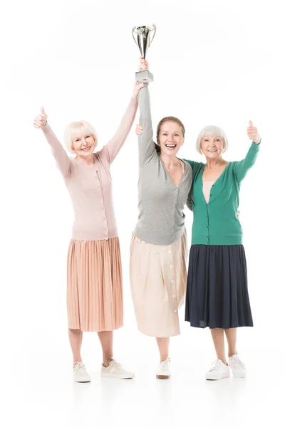 Tres mujeres elegantes sonrientes celebrando con copa de trofeo aislada en blanco - foto de stock