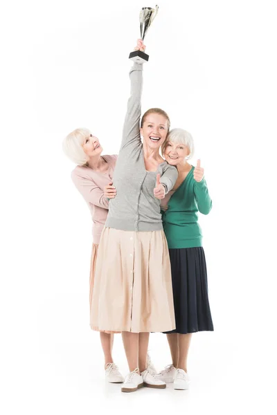 Happy stylish women showing thumb up gesture and celebrating with trophy isolated on white — Stock Photo