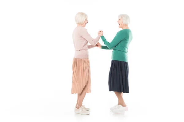 Vista lateral de dos mujeres con estilo senior tomados de la mano el uno del otro aislados en blanco - foto de stock