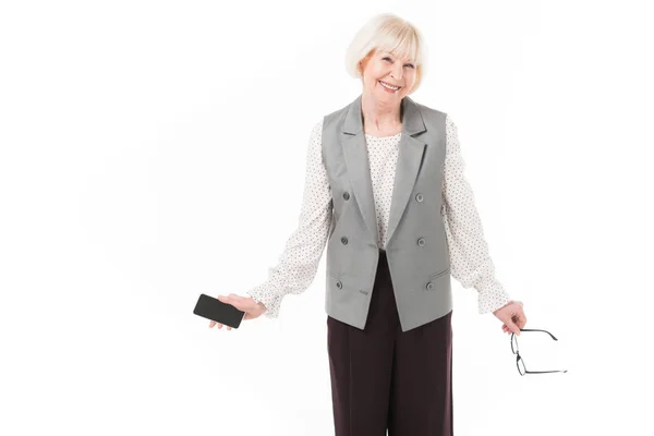 Femme d'affaires élégante senior tenant smartphone et lunettes isolées sur blanc — Photo de stock