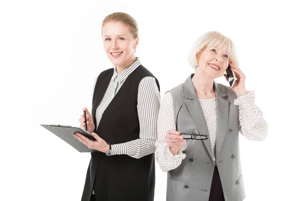 Стильная старшая деловая женщина разговаривает по смартфону, в то время как зрелая бизнесвумен держит планшет изолированным на белом — стоковое фото