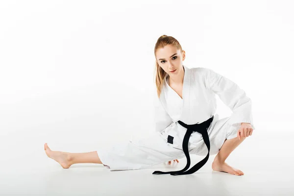 Female karate fighter stretching and looking at camera isolated on white — Stock Photo