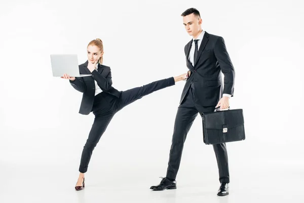 Businesswoman holding laptop and kicking businessman isolated on white — Stock Photo