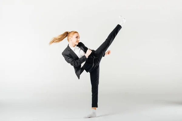 Businesswoman performing kick in suit isolated on grey — Stock Photo