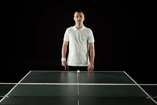 Retrato de jugador de tenis en uniforme de pie en la mesa de tenis con pelota aislada en negro — Stock Photo