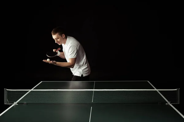 Tennisspieler mit Tennisschläger und Ball in der Hand steht isoliert auf schwarz an der Tischtennisplatte — Stockfoto