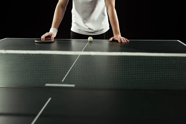 Cropped shot of tennis player leaning on tennis table with racket and ball isolated on black — Stock Photo