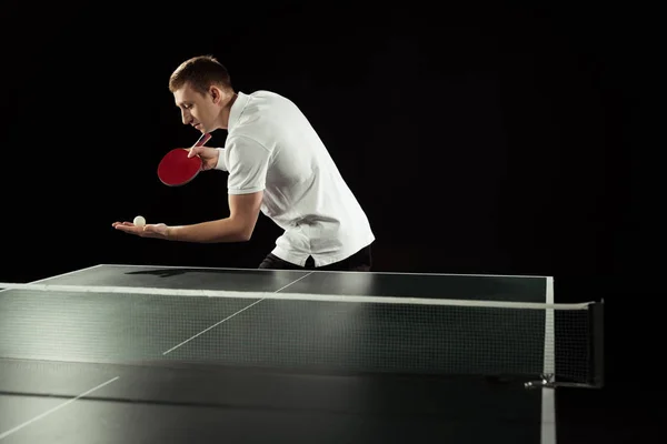 Jugador de tenis con raqueta de tenis y pelota en las manos de pie en la mesa de tenis aislado en negro — Stock Photo