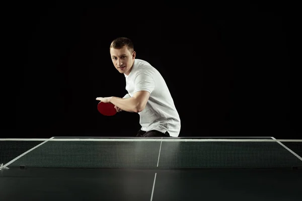 Joven tenista en uniforme practicando tenis de mesa aislado sobre negro — Stock Photo