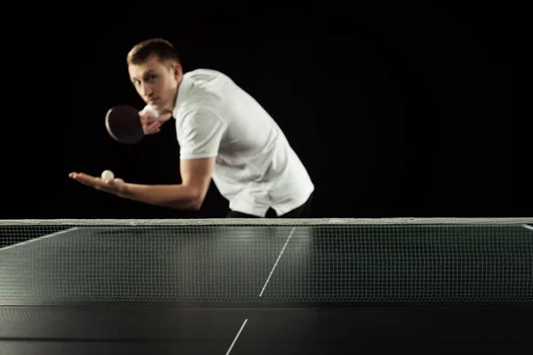 Selective focus of tennis player with tennis racket and ball in hands standing at tennis table isolated on black — Stock Photo