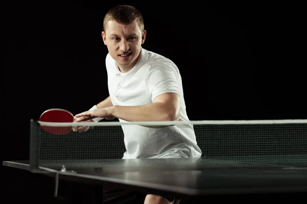Young emotional tennis player in uniform practicing in table tennis isolated on black — Stock Photo