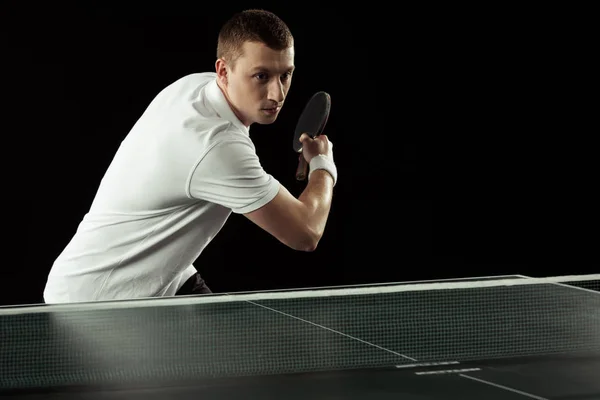 Young focused tennis player in uniform practicing in table tennis isolated on black — Stock Photo