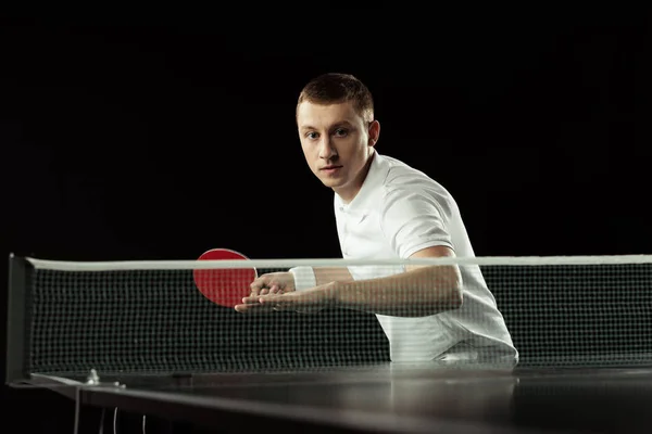 Young focused tennis player in uniform practicing in table tennis isolated on black — Stock Photo