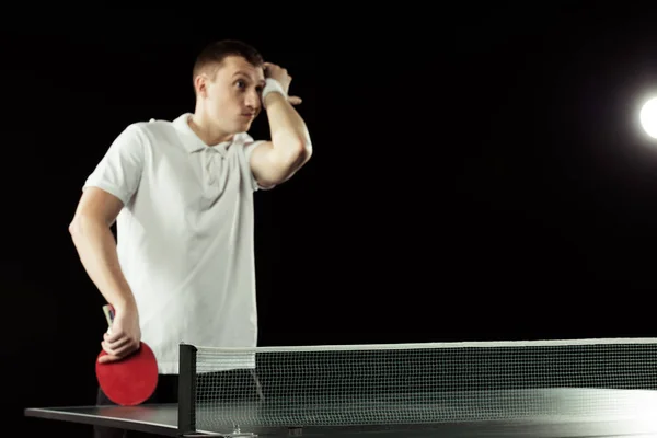 Tenista cansado en uniforme cerca de la mesa de tenis aislado en negro — Stock Photo