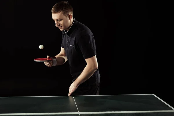 Tennis player in uniform practicing with racket and ball isolated on black — Stock Photo