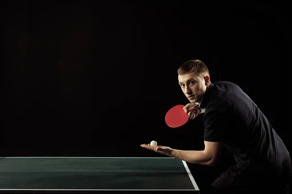 Vista lateral del joven tenista de mesa con raqueta y pelota en manos aisladas en negro - foto de stock