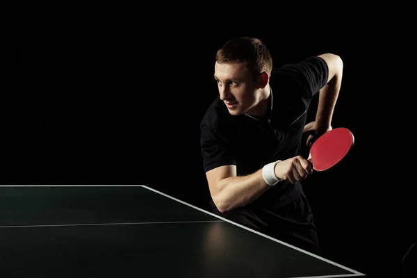 Vue latérale du jeune joueur de tennis pratiquant dans le tennis de table isolé sur noir — Photo de stock