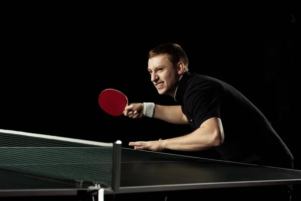 Vue latérale du joueur de tennis émotionnel pratiquant dans le tennis de table isolé sur noir — Photo de stock