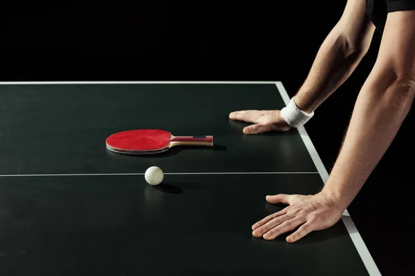 Частковий вид тенісиста, що спирається на тенісний стіл з ракеткою і м'ячем ізольовано на чорному — стокове фото