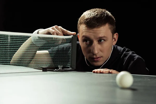 Portrait of focused tennis player checking net on tennis table isolated on black — Stock Photo