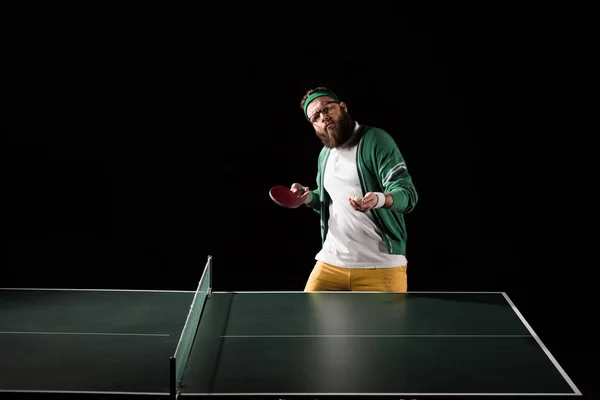 Sportif barbu avec équipement de tennis debout à la table isolé sur noir — Photo de stock