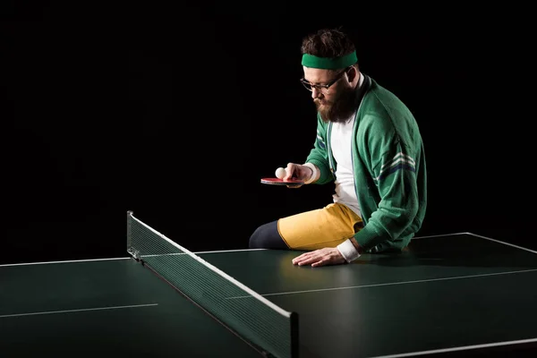 Joueur de tennis barbu avec raquette et balle assis sur la table de tennis isolé sur noir — Photo de stock