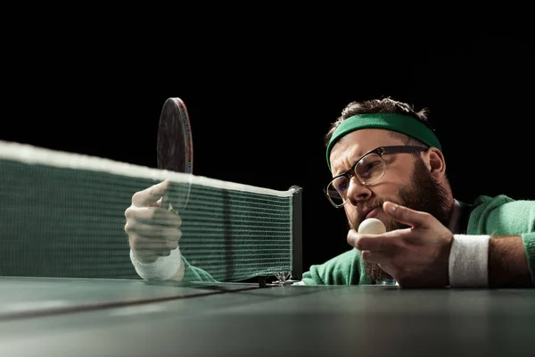 Pensive bearded tennis player looking at racket in hand isolated on black — Stock Photo