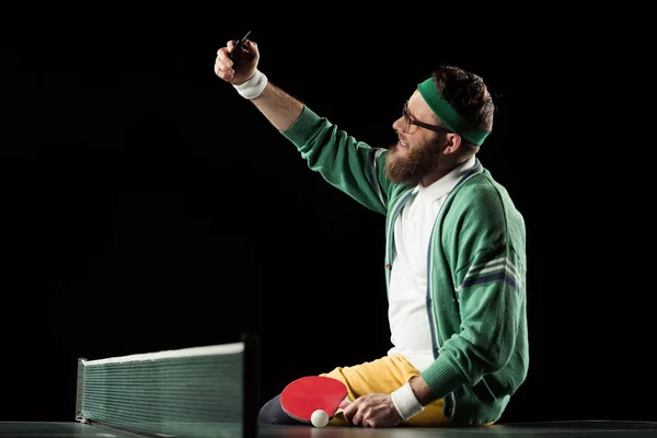 Joueur de tennis souriant prenant selfie sur smartphone sur table de tennis isolé sur noir — Photo de stock