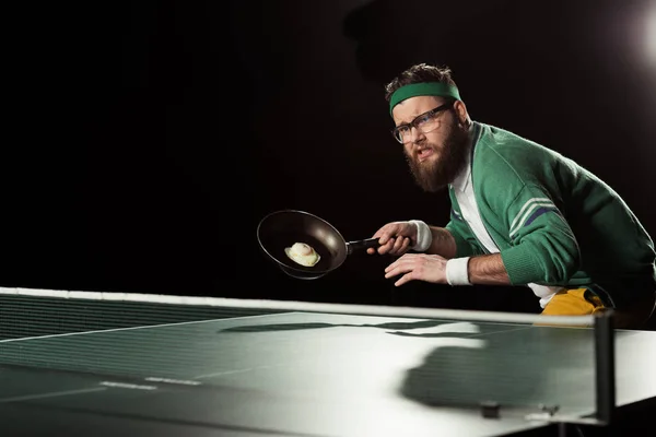 Joueur de tennis avec poêle à frire avec oeuf jouer au tennis de table isolé sur noir — Photo de stock