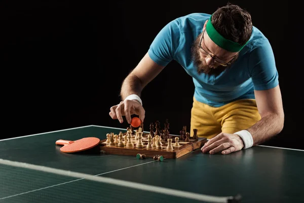Tennis player putting ball on chess board on tennis table isolated on black — Stock Photo
