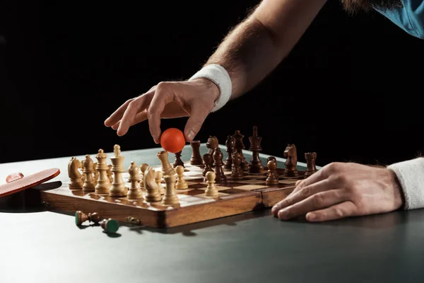Partial view of tennis player putting tennis ball on chess board with figures isolated on black — Stock Photo