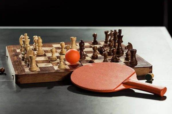 Vista de perto de raquete de tênis, bola e tabuleiro de xadrez com figuras na mesa de tênis — Fotografia de Stock