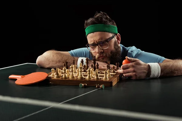 Pensive bearded man looking at chess board on tennis table isolated on black — Stock Photo