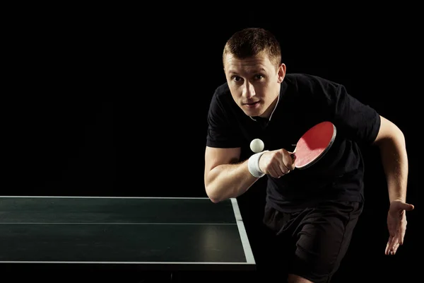 Retrato de jugador de tenis enfocado jugando tenis de mesa aislado en negro - foto de stock