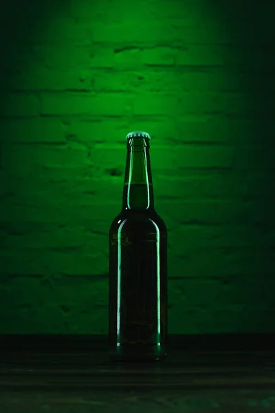 Vista de cerca de una sola botella de cerveza verde en luz verde - foto de stock