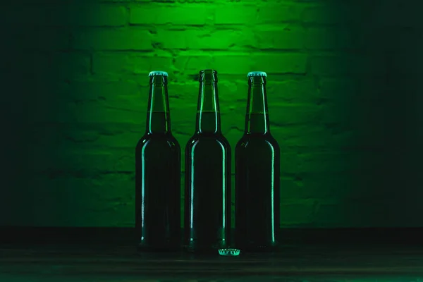 Trois bouteilles de bière verte près du mur de briques vertes — Photo de stock