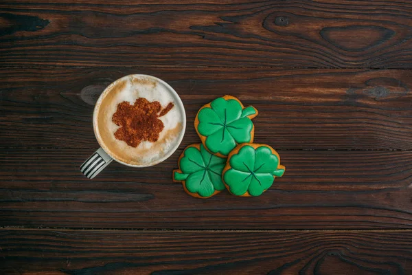 Top view of cappuccino and cookies in shape of shamrocks on wooden table — Stock Photo