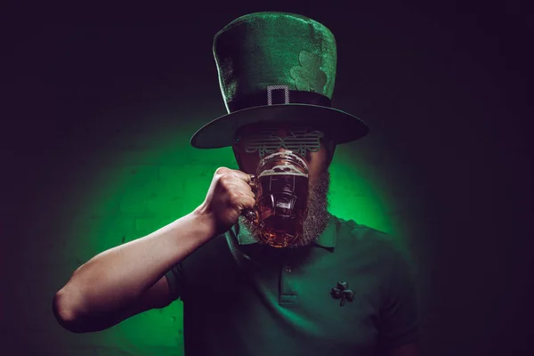 Young bearded man in green irish hat drinking beer — Stock Photo