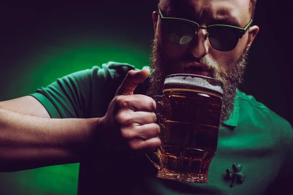Homme barbu dans des lunettes de soleil et un polo vert boire de la bière — Photo de stock