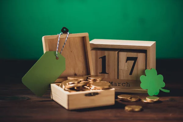 Vista ravvicinata del calendario, simbolo verde trifoglio, etichetta bianca e monete d'oro sul tavolo di legno — Foto stock