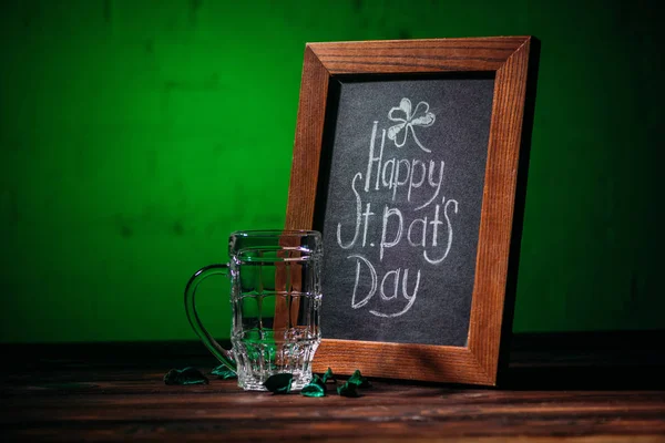 Marco de madera con feliz día de San Patricio inscripción y vaso de cerveza vacío en la mesa - foto de stock