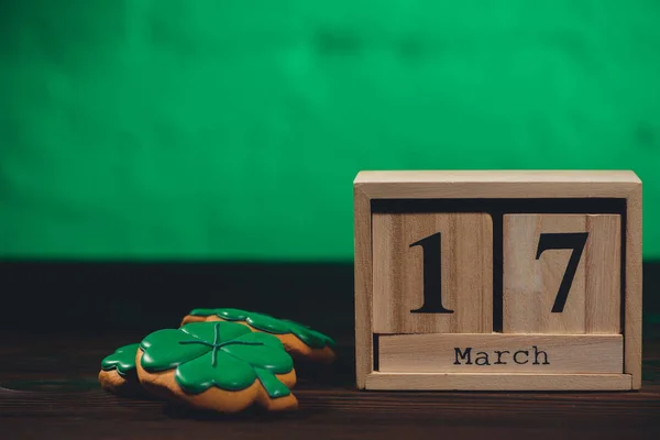 Close-up view of calendar with 17 march date and cookies and hsape of shamrocks on wooden table top — Stock Photo