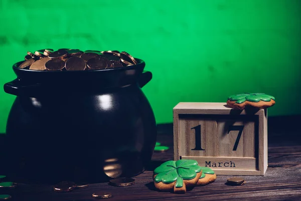 Calendário, biscoitos em forma de trevo e panela com moedas de ouro na mesa de madeira — Fotografia de Stock