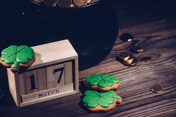 Vista close-up do calendário, biscoitos em forma de trevo e panela com moedas de ouro na mesa de madeira — Fotografia de Stock