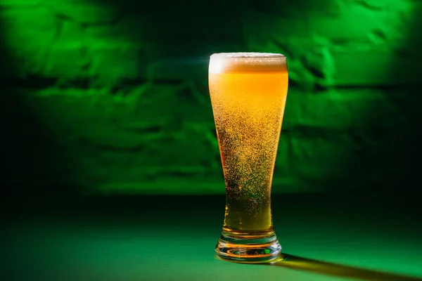 Close-up view of glass with fresh cold amber beer in green light, saint patricks day concept — Stock Photo