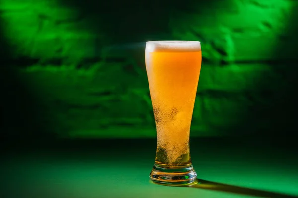 Close-up view of glass with beer in green light, saint patricks day concept — Stock Photo