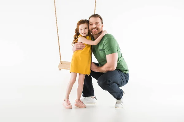 Дочь, стоящая рядом с качелями и обнимающая отца, изолированная на белом — стоковое фото