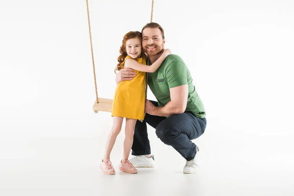 Figlia in piedi vicino altalena e abbracciando padre isolato su bianco — Foto stock